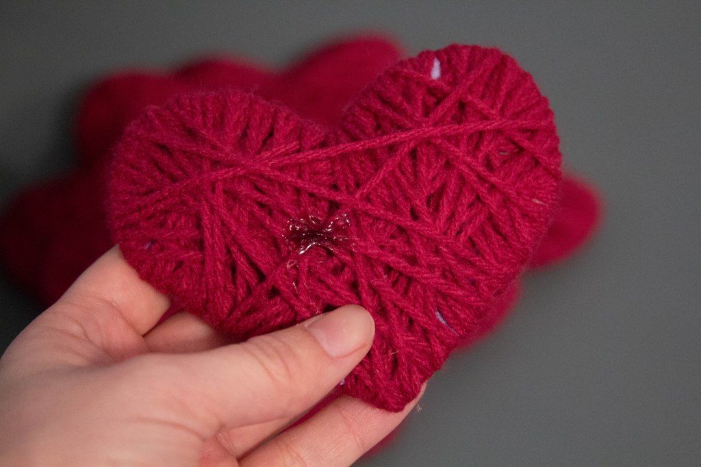 Hot gluing the end of yarn to a cardboard heart. 
