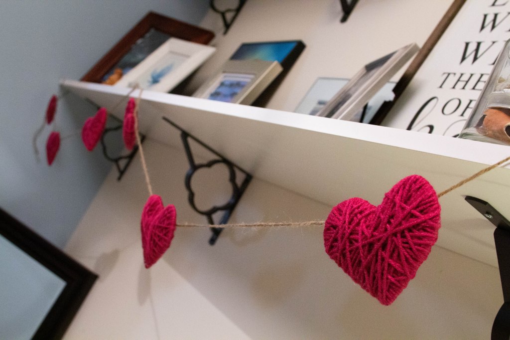 Pink yarn heart garland hanging from shelves. 