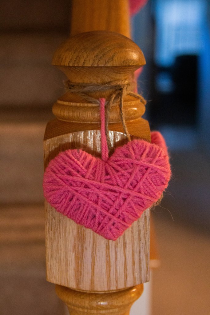 Pink yarn heart garland hanging from stair banister. 