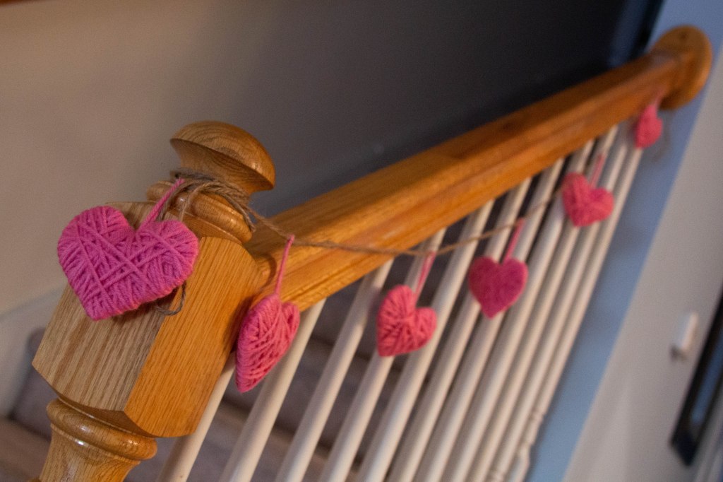 Pink yarn heart garland hanging from stair banister. 